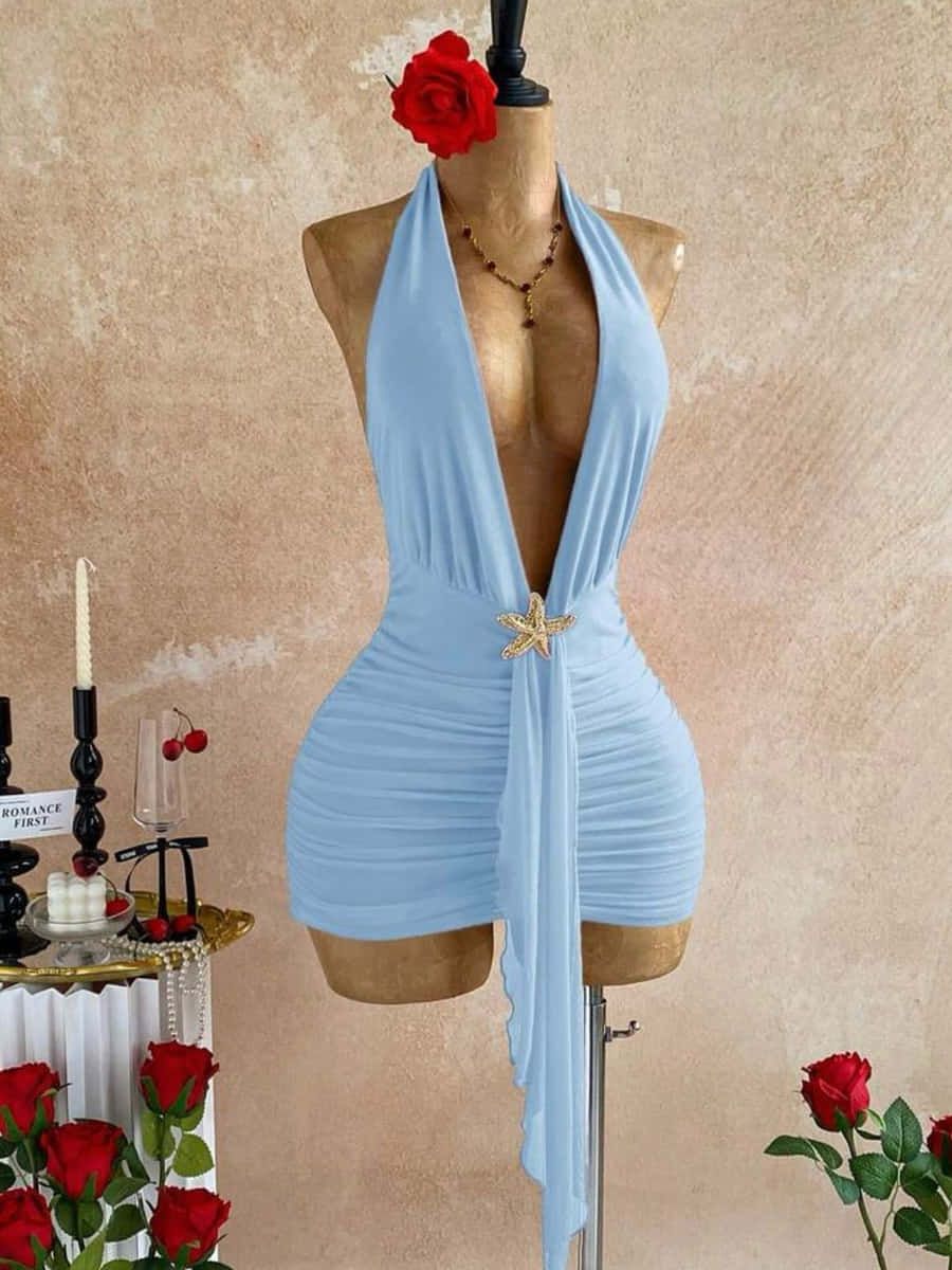 Vestido corto celeste con escote halter profundo, falda drapeada y broche dorado de estrella de mar
